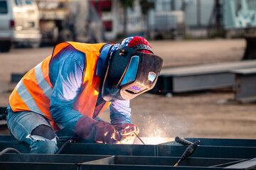 Worker welder on a construction site with an orange vest and a welding mask, working on welding