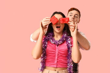 Young couple with Christmas tinsel and gift boxes on pink background