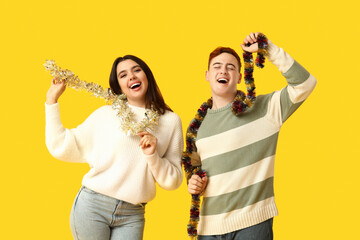 Happy young couple with Christmas tinsel on yellow background