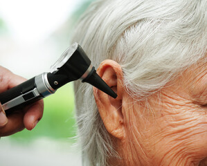 Otolaryngologist or ENT physician doctor examining senior patient ear with otoscope, hearing loss problem. .