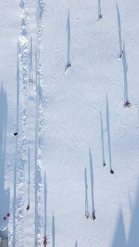 Top view of skiers and snowboarders skiing on a snow slope with a ski lift at the ski resort on a sunny day.