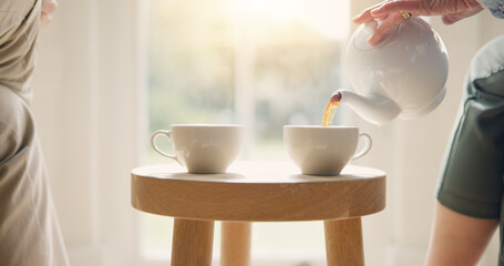 Pot, pour and hands with tea cup in morning, home and closeup on drink, steam and table. Hot,...