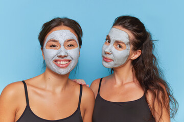 Two brunette friendgirls having fun while making skin care procedure with clay facial masks, healthcare products concept, copy space