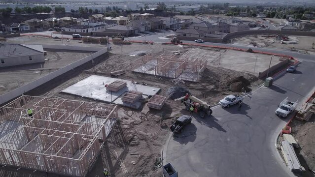 A drone elegantly circles a telehandler, poised and awaiting instructions on a bustling home construction site, capturing the precision and readiness of construction equipment in action