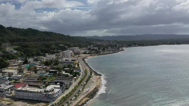 High drone footage of cars driving on coastal roads and seafront buildings in Aguadilla, Puerto Rico