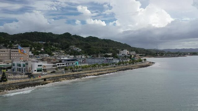 Drone footage of cars driving on coastal roads and seafront buildings in Aguadilla, Puerto Rico