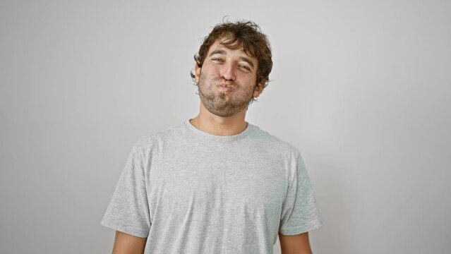 Cheeky young guy in a t-shirt making a hilarious grimace, puffing cheeks full of air for a crazy fun face. standing isolated, he breathes life into the white background.