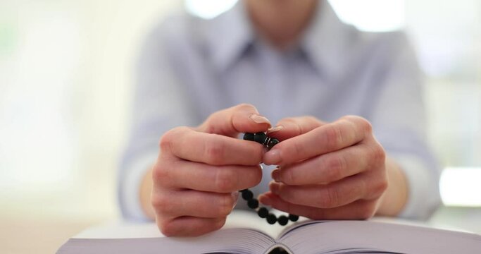 Woman prays with Bible on table and holds black rosary