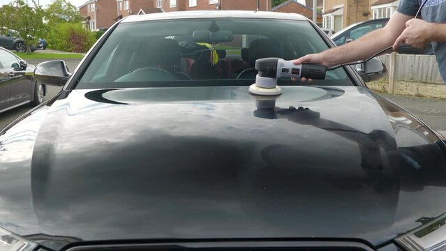 Polishing a black car bonnet hood with a machine polisher