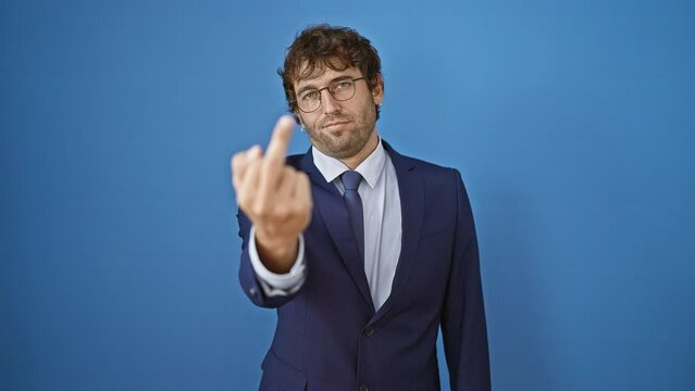Young man wearing business suit showing middle finger, impolite and rude fuck off expression over isolated blue background