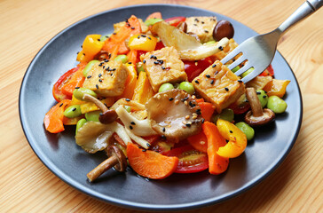 Closeup of Fork Scooping Roasted Tempeh Cube from Colorful Vegan Salad Dish