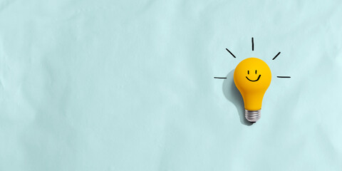 Naklejka premium Yellow light bulb with happy face - flat lay