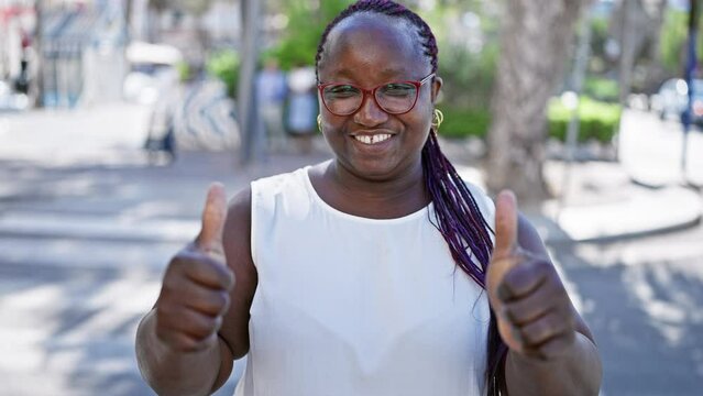 Joyful, confident african american woman flashing a fun, approving thumbs-up sign on a sunny city street, her cool glasses gleaming.