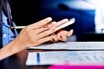 Close-up of a woman's hand holding a pen while using a cell phone to check marketing information in an office meeting room
