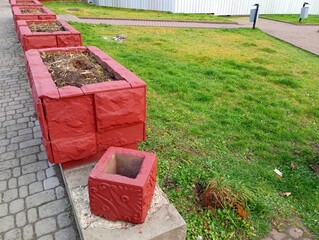 Concrete square flower beds serve as a barrier between the lawn and the sidewalk. City square with flower beds and green lawn in autumn.