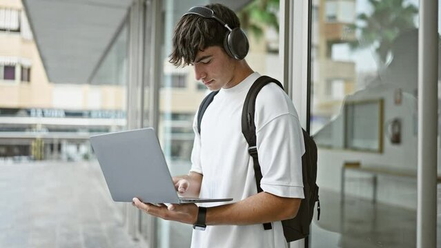 Cool young hispanic dude, a smart university student, lost in music through laptop, chilling outdoors on campus