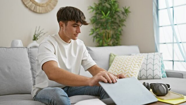 Young hispanic teenager finishing study session, lying relaxed on home sofa, engrossed in technology.