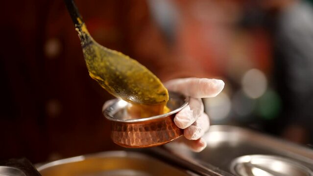 cook pouring spicy sauce in gravy boat, closeup view, professional on kitchen of Asian restaurant