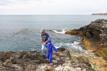 Fototapeta premium A man with a child on Cape Tarkhankut. The rocky coast of the Dzhangul Reserve in the Crimea. Turquoise sea water. Rocks and grottoes of Cape Tarkhankut on the Crimean peninsula.