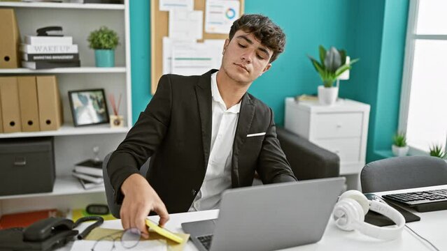 Young Hispanic Teenager Business Worker Using Laptop And Smartphone At The Office