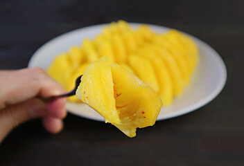Closeup fork picking up a piece of fresh pineapple with blurry slices in the backdrop