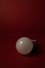 White light bulb on burgundy background, dark key