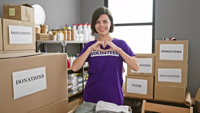 With hands forming a love symbol, a young, beautiful hispanic woman with short hair confidently volunteer at a charity center, her radiant smile reflecting the joy of selfless service.