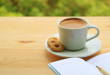 Cup of Hot Coffee and Cookies with Lined Note Papers on Wooden Table with Blurry Green Foliage in the Backdrop