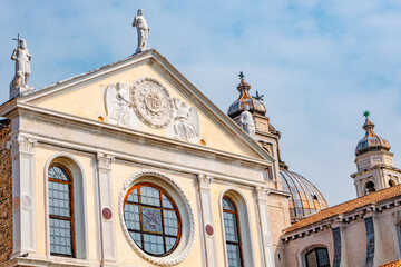 Fototapeta na wymiar Venice, Italy. Ancient roof statues at facade Chiesa di Santa Maria della Visitazione Church at sunny day and blue sky