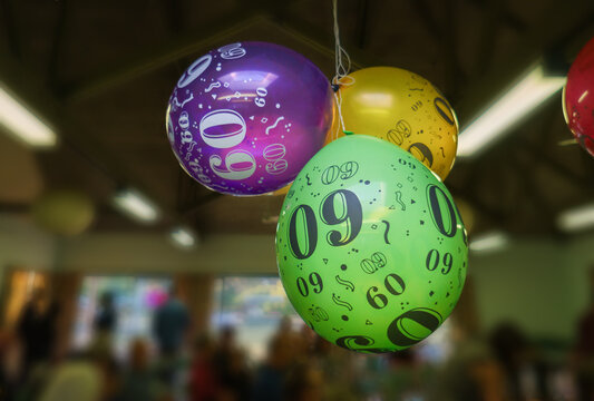 60th birthday balloons hanging from the ceiling. Unrecognizable people gathering in the room. Birthday celebration.