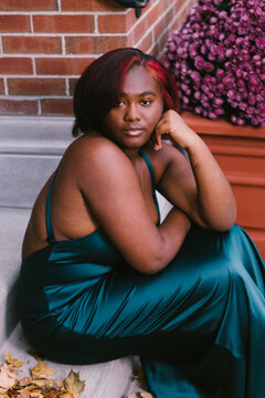 Feminine black person sits on step in green formal dress