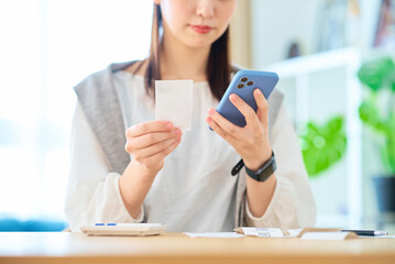レシートとスマートフォンを手にする若い女性
