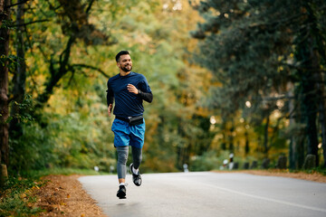 Happy athletic man running on road in nature.