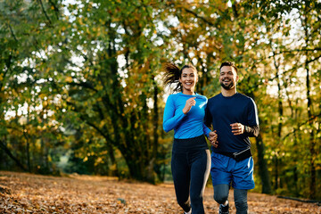 Happy couple of athletes running in autumn day in nature.