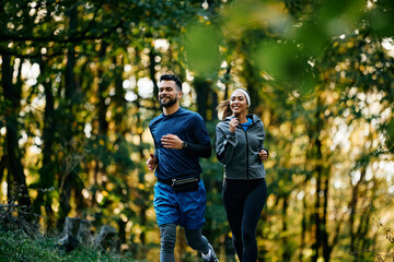 Young happy athletic couple running while exercising in nature.