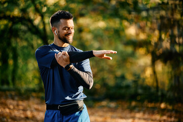 Happy athlete stretching his arms while having sports training in park.