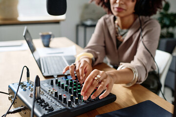 Focus on hand of young woman turning consoles of soundboard while adjusting equipment before making...