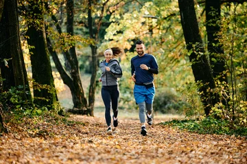 Poster Young athletic couple jogging during autumn day in park. © Drazen