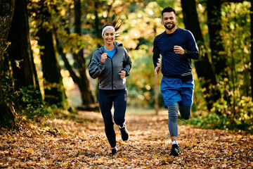Happy athletic couple jogging through nature during autumn day