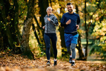 Happy couple of athlete running in park in autumn.