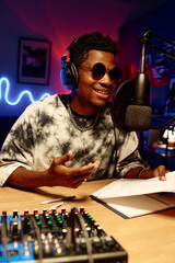 Young smiling man in sunglasses and headphones speaking in microphone while reading points of...