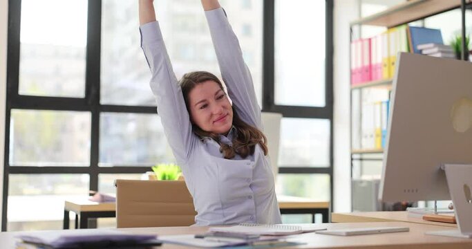Attractive young woman stretches at workplace and smiles in office