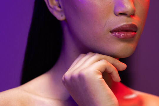 Fototapeta Close up of biracial woman with dark hair, red lips and hand to face on neon background