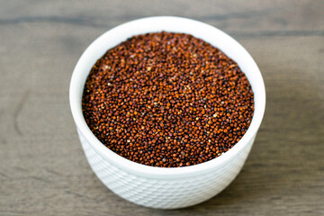 Red quinoa on the white plate on the wooden background. Healthy food and nutrition concept. Safe, ecological, and healthy products