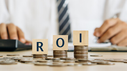 ROI,Return On Investment concept.ROI word on wooden block on stack coin with home model...