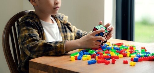 Little boy playing rubik's cube in hands and kid toy on table, Brainstorming making logic solution.