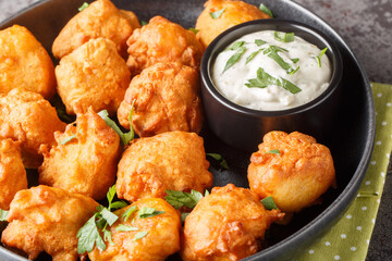 Southern Hush Puppies are light and flakey cornmeal dough that is fried golden brown on the outside and soft on the inside closeup on the plate on the table. Horizontal