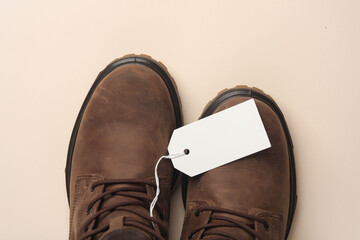 Winter leather boots with white blank tag on a string, beige background. Template for design, sale,...