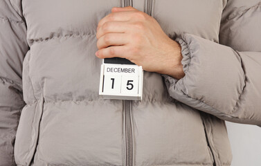 Man in down jacket holds wooden block calendar with date December 15