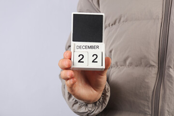 Man in down jacket holds wooden block calendar with date December 22